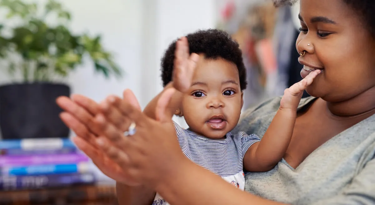A caregiver playing patty-cake with a smiling baby